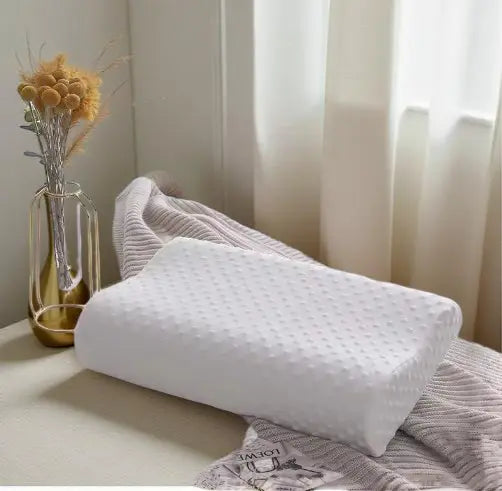 White ergonomic memory foam pillow for neck support on bed with gray blanket and vase of flowers